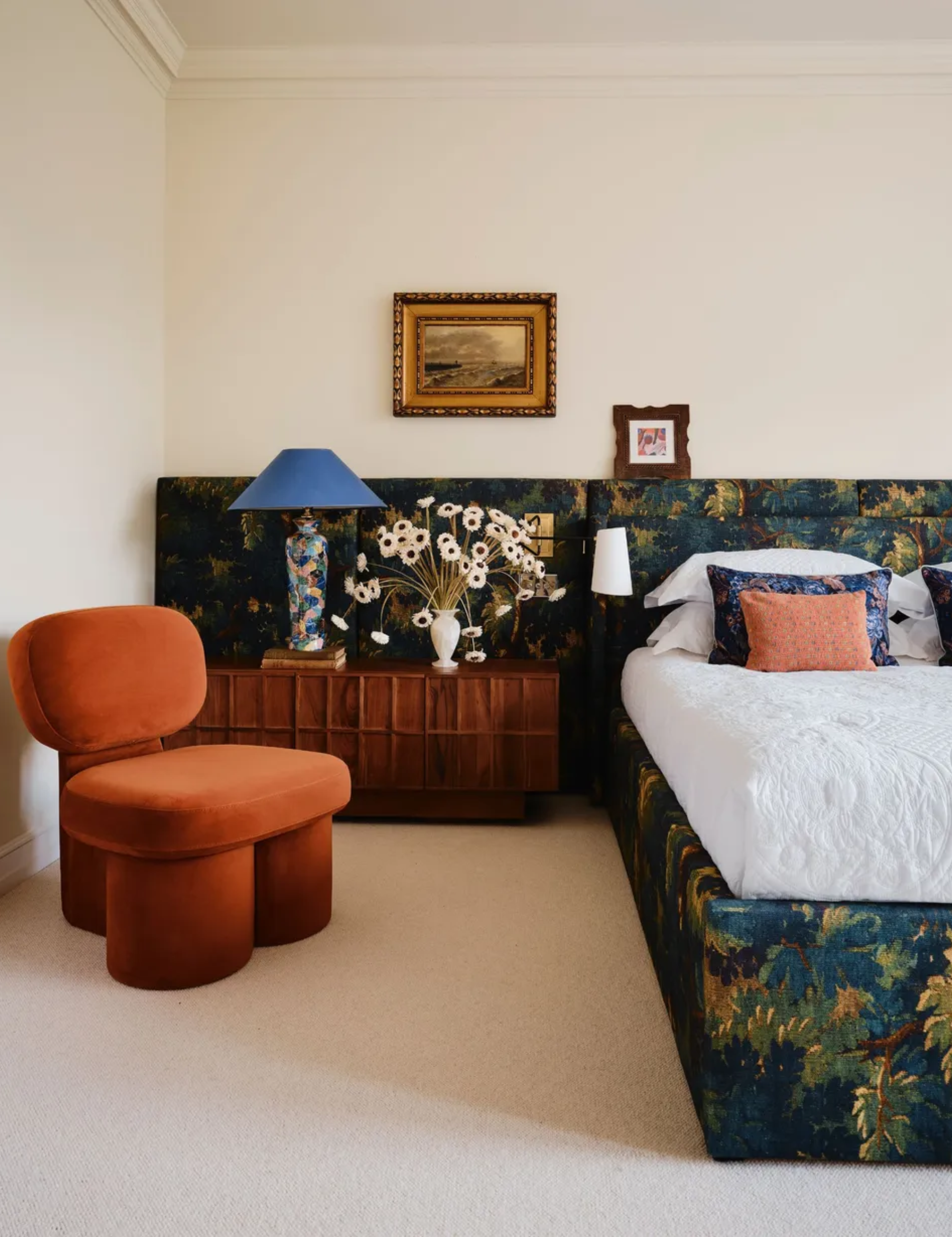 neutral bedroom with a wide wall-to-wall upholstered headboard in a green tapestry leafy print accessories with vintage furniture