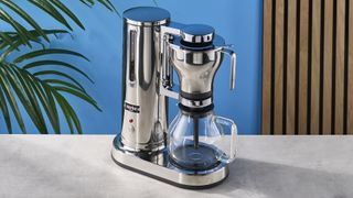 a silver drip brew coffee maker with a 10 cup capacity is photographed against a blue background