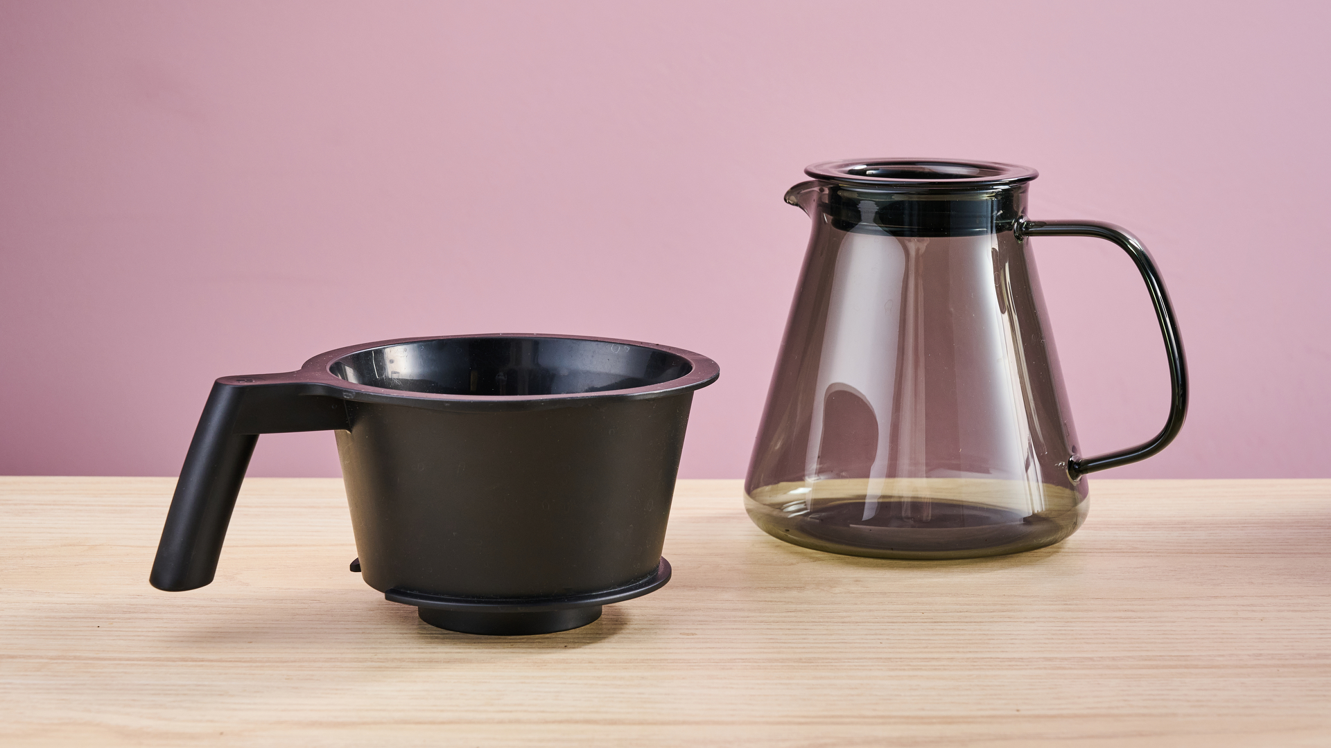 The Ratio Four's carafe and filter basket on a desk in front of a pink background.