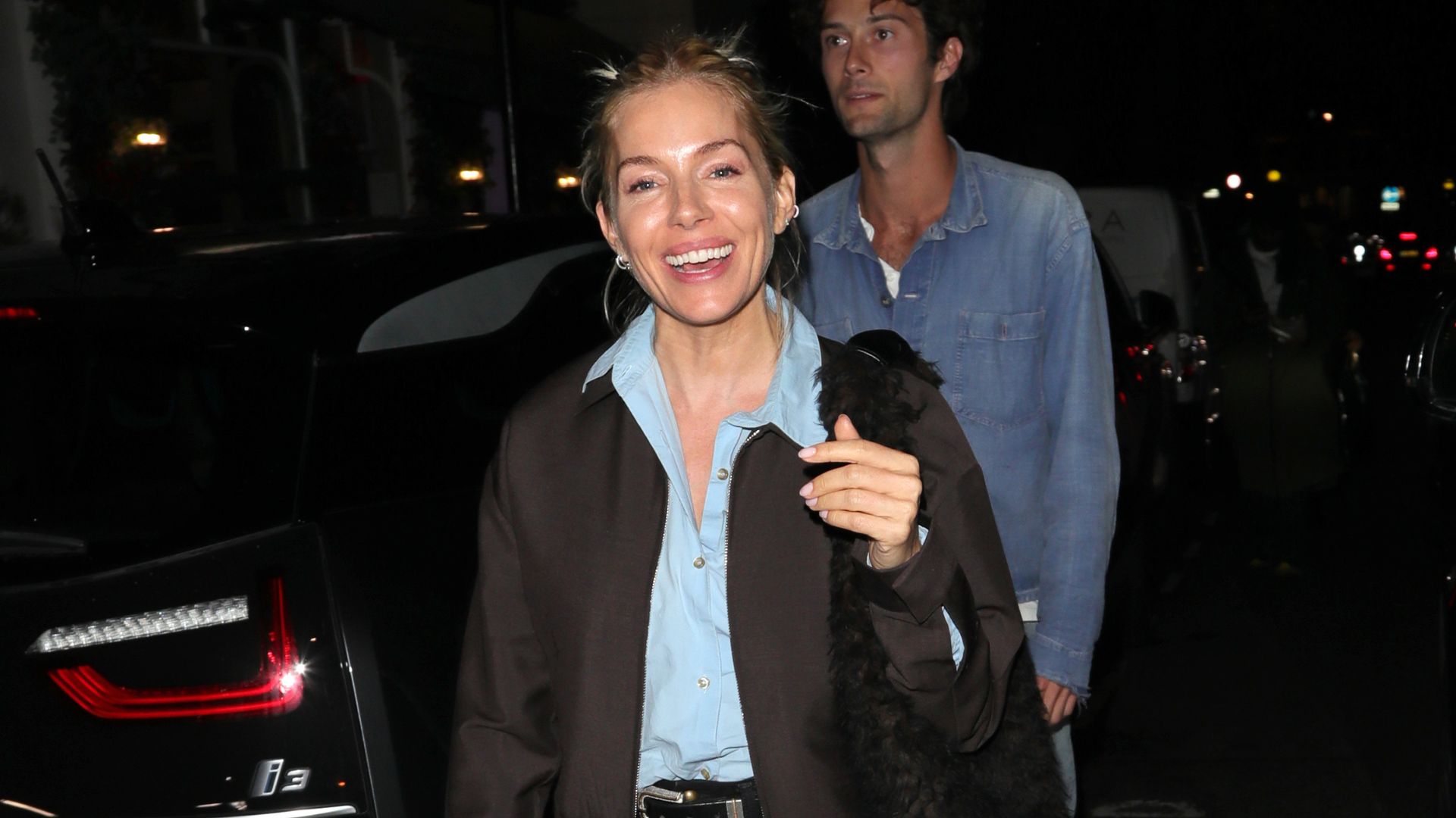 Sienna Miller steps out in London wearing black jeans with square-toe flats, a blue shirt and a dark brown jacket.