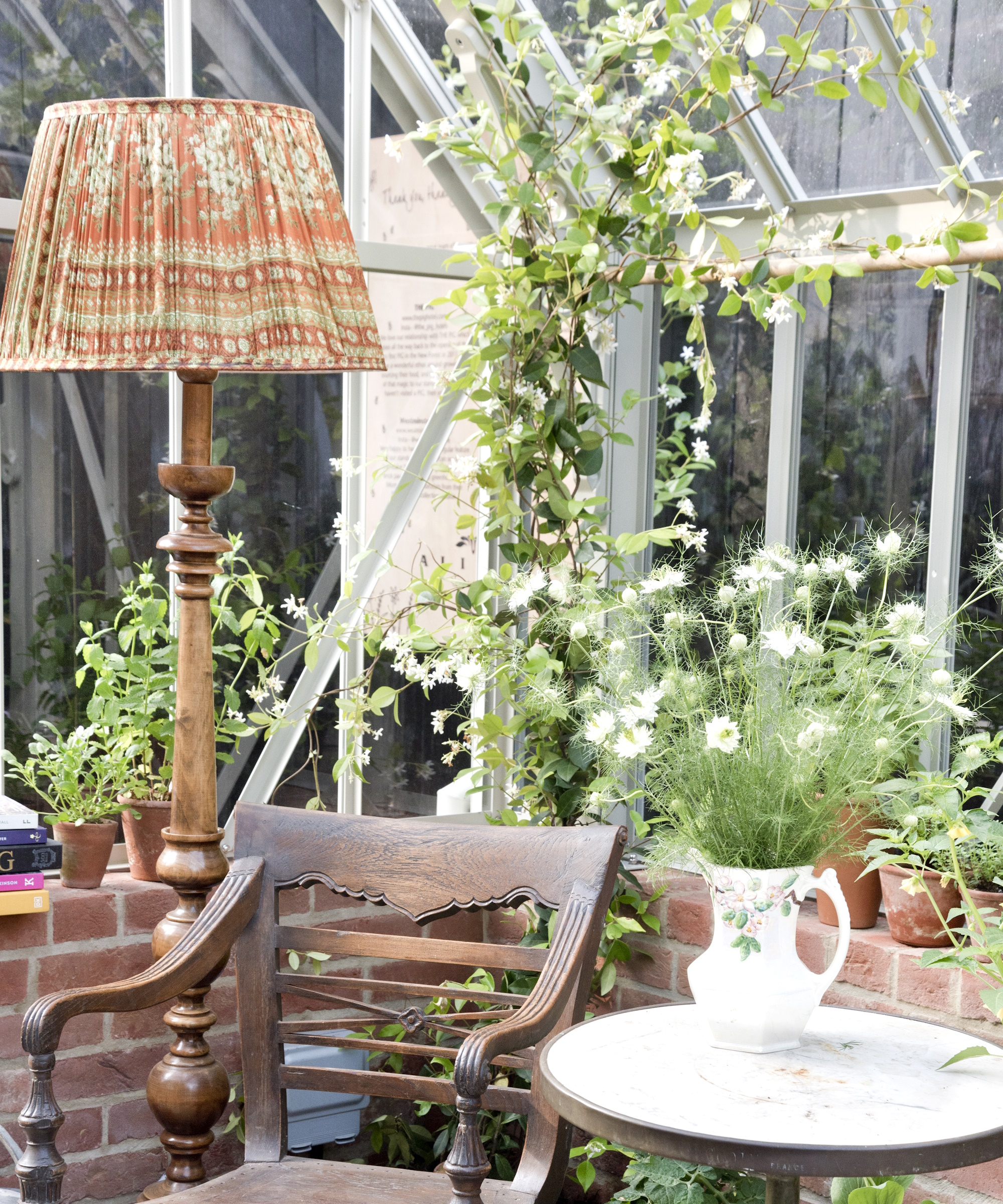 Wooden antique chair, lamp and side table with a jug full of nigella flowers in the corner of a greenhouse