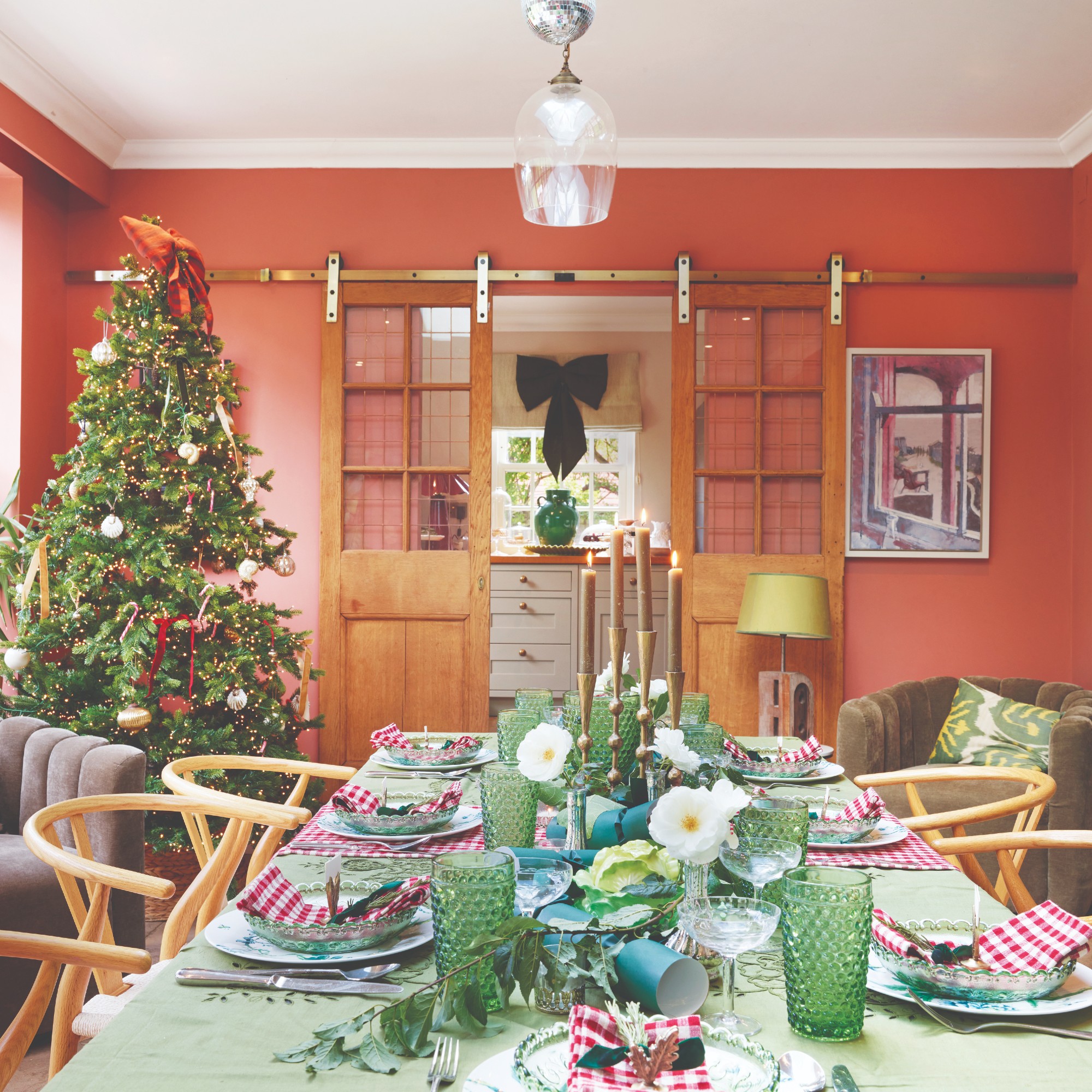 A coral-painted dining room with a set table and a decorated Christmas tree in the corner