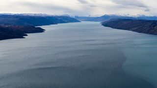 An aerial photo of a wide fjord with mountains in the background