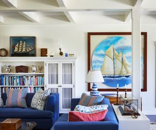 beamed living room with fire lit, blue sofas red and blue patterned cushions and boat pictures