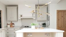 Minimalist kitchen island ideas are so chic. Here is a kitchen with a white kitchen island with two wooden stools in frotn of it, a gold sputnik chandelier above it, and light gray cabinets and drawers behind it