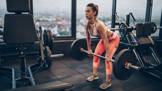 Woman performs Romanian deadlift in a gym with a barbell