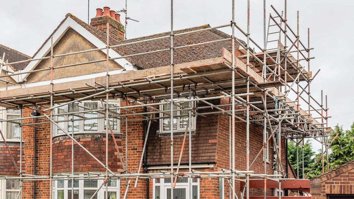 1930s semi detached clad in brick and render, surrounded by scaffolding and undergoing renovation.