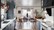 main kitchen diner with navy cabinets. wooden floor, white range, wooden dining table, wooden and metal chairs 