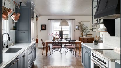 main kitchen diner with navy cabinets. wooden floor, white range, wooden dining table, wooden and metal chairs 