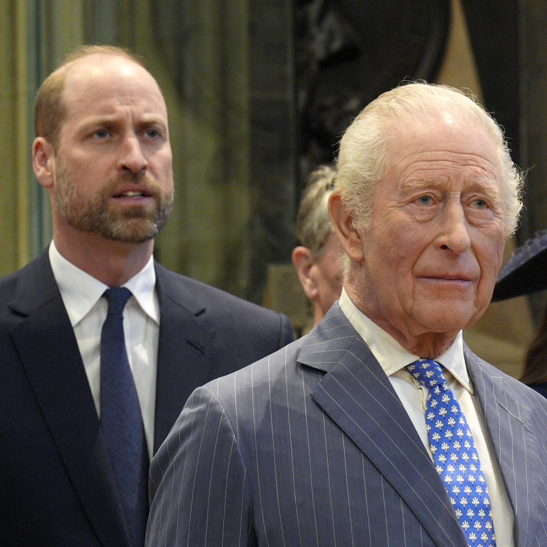 King Charles standing in front of Prince William, both wearing suits and ties