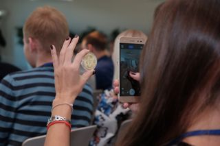 A woman taking a picture of a bitcoin on her phone in a classroom