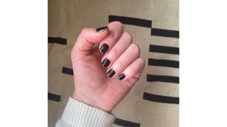 A close-up picture of Digital Beauty Editor, Fiona McKim's hand with a short, glossy black manicure/ against a black and cream fabric background