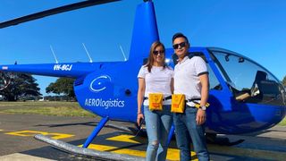couple stands in front of a blue helicopter