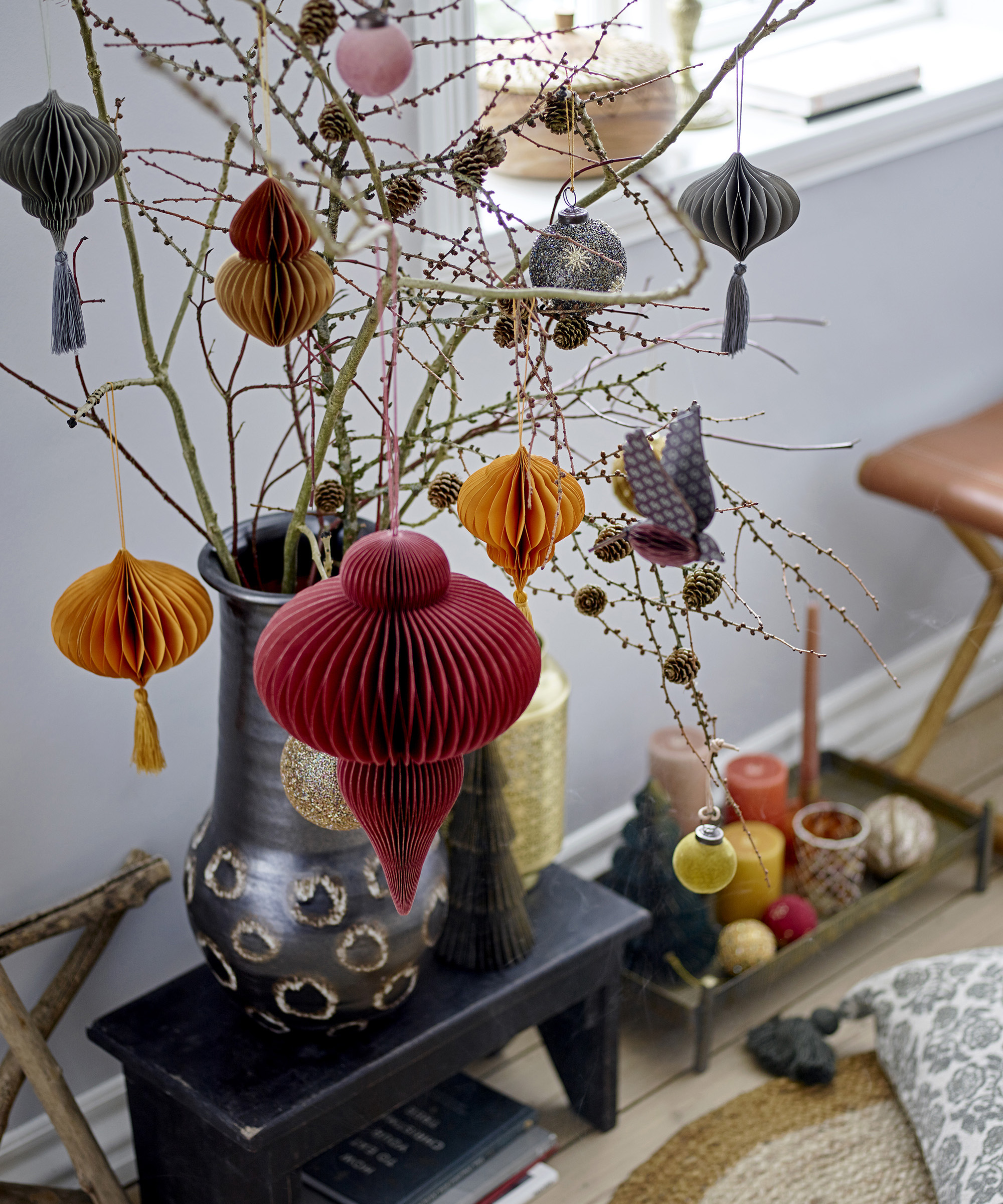 A living room with vase by window with branches and paper honeycomb decorations