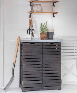 storage cabinet with grey slatted front and gardening fork leaning against the side