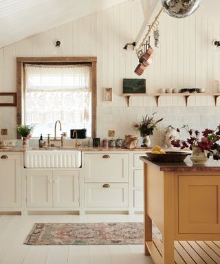 country style kitchen with turmeric colored kitchen island, shiplap walls and ceiling, rug, lace net curtain, fluted sink, open shelving