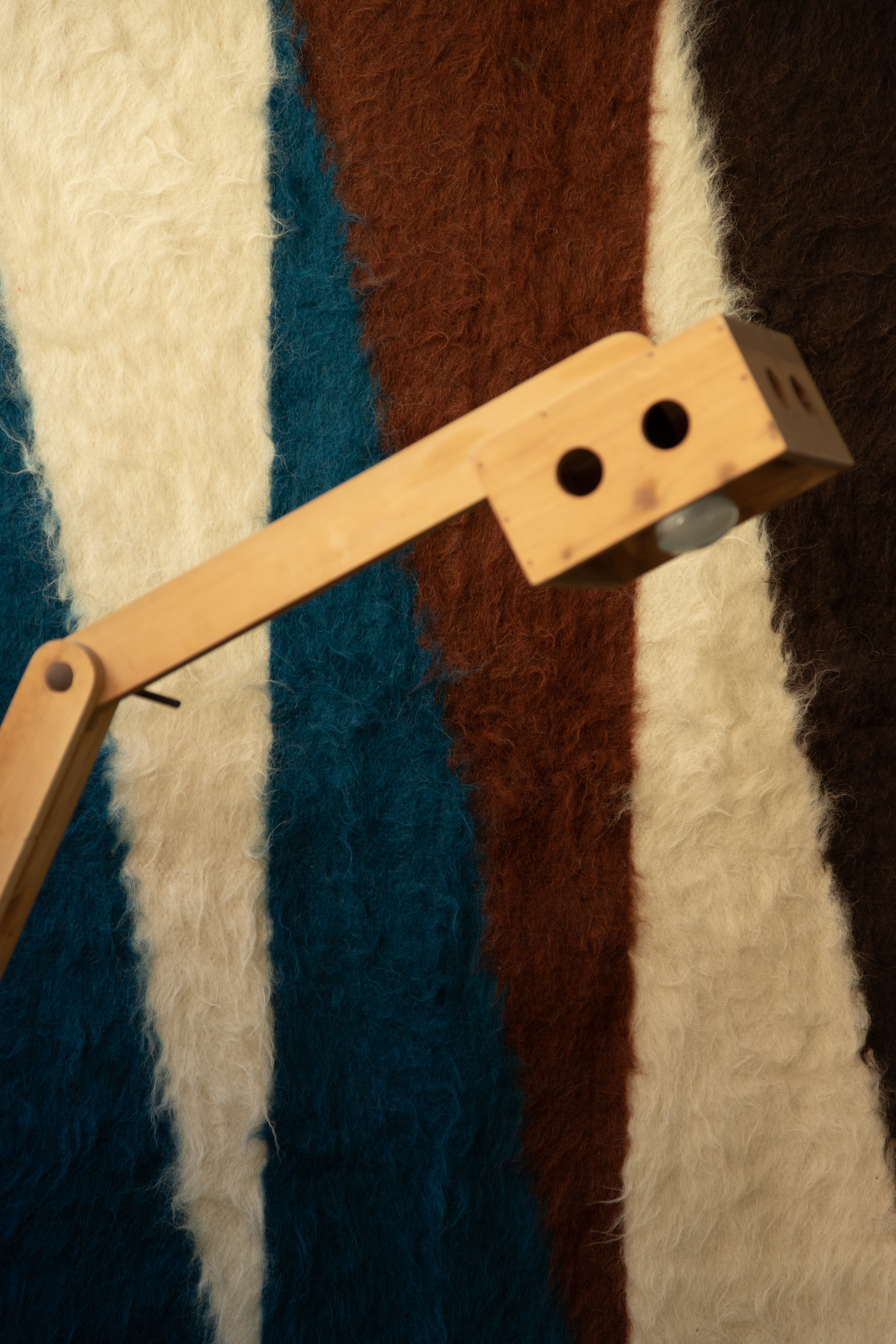 A wool tapestry in terracotta, blue, and white hangs at the back of a geometric wooden standing lamp.