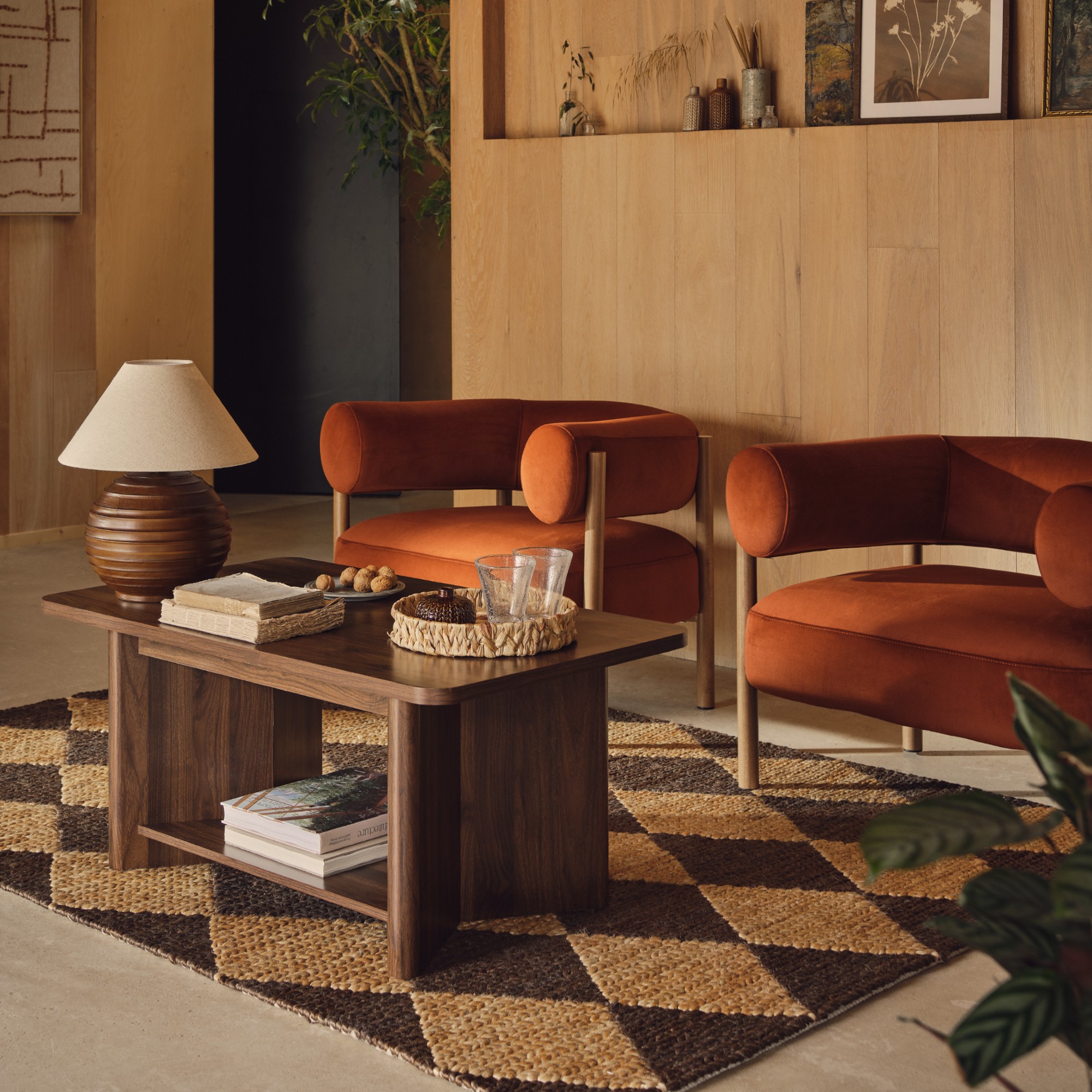 A living room with two matching armchairs in rust velvet with a diamond-pattern jute rug underneath
