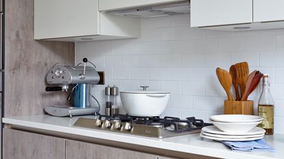 A white kitchen with a silver coffee machine and a vase of foliage