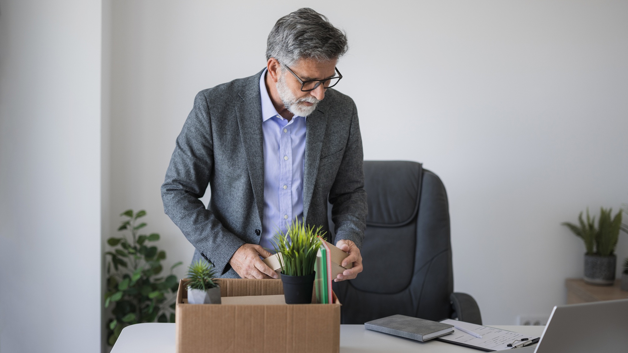 An older man packs up belongings at his desk.