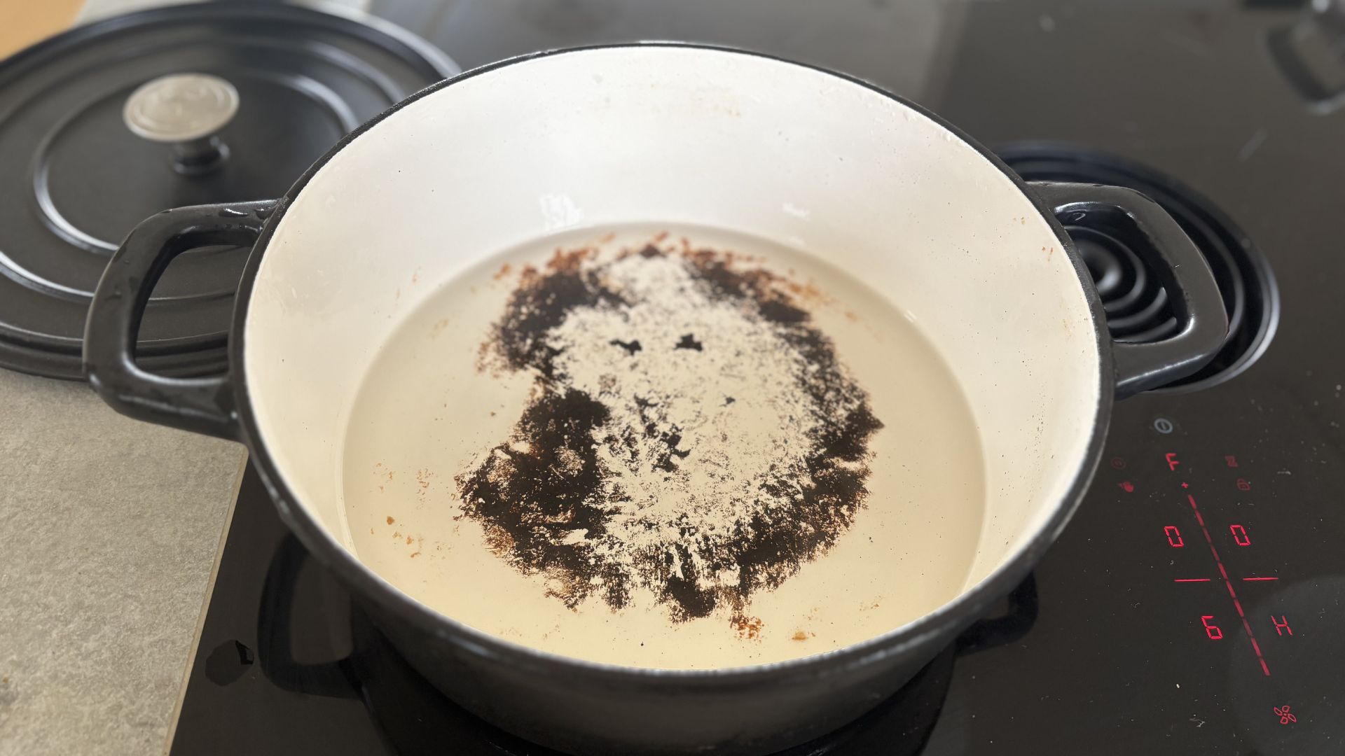 A stage of cleaning a burnt cast iron casserole dish on a hob