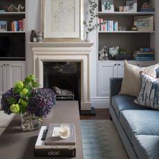 A living room with a light blue velvet sofa and a rectangular coffee table with a vase of hydrangeas and a stack of coffee table books