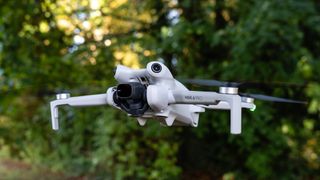 Dji Mini 4 Pro in flight in front of trees