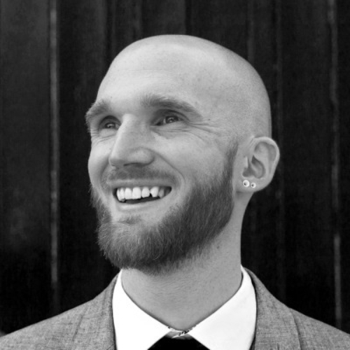 Black and white image of a man smiling in a light suit.