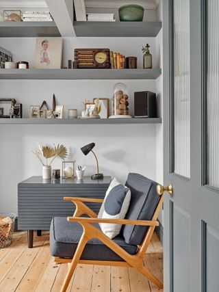 White living room with grey painted open shelving and a mid-century armchair with grey seat cushions