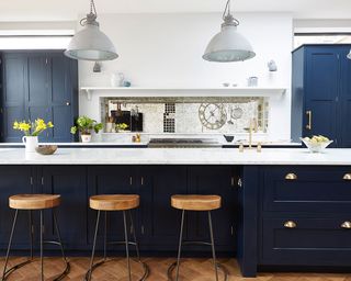 An example of kitchen extension ideas showing a dark blue island with wooden bar stools and white pendant lamps above