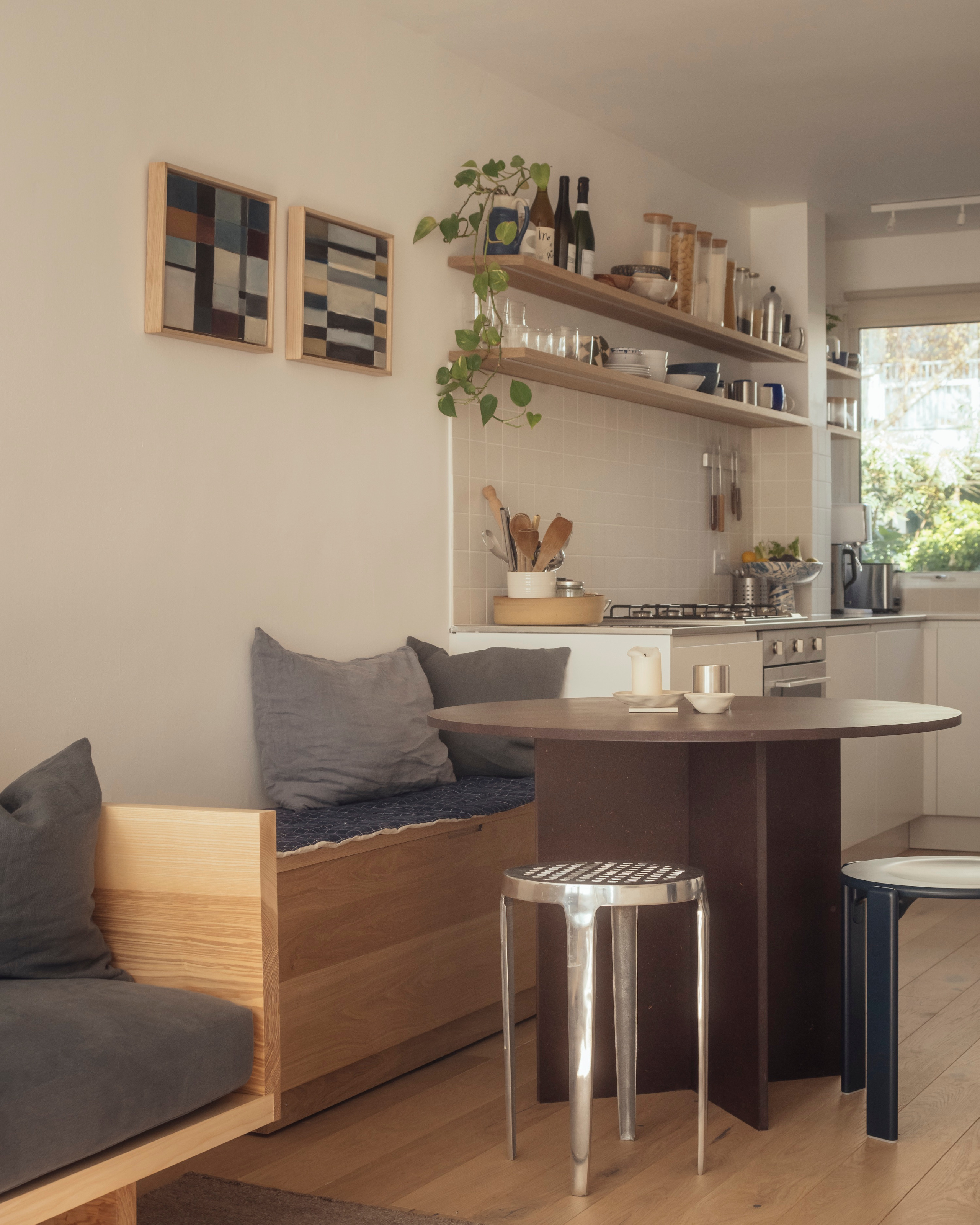Bench seating built into the edge of a kitchen with a round dining table and two steel stools
