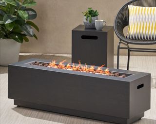 GDF Studio Jaxon Outdoor 50,000 BTU Rectangular Fire Table with Tank Holder, Dar lifestyle image outside with chair