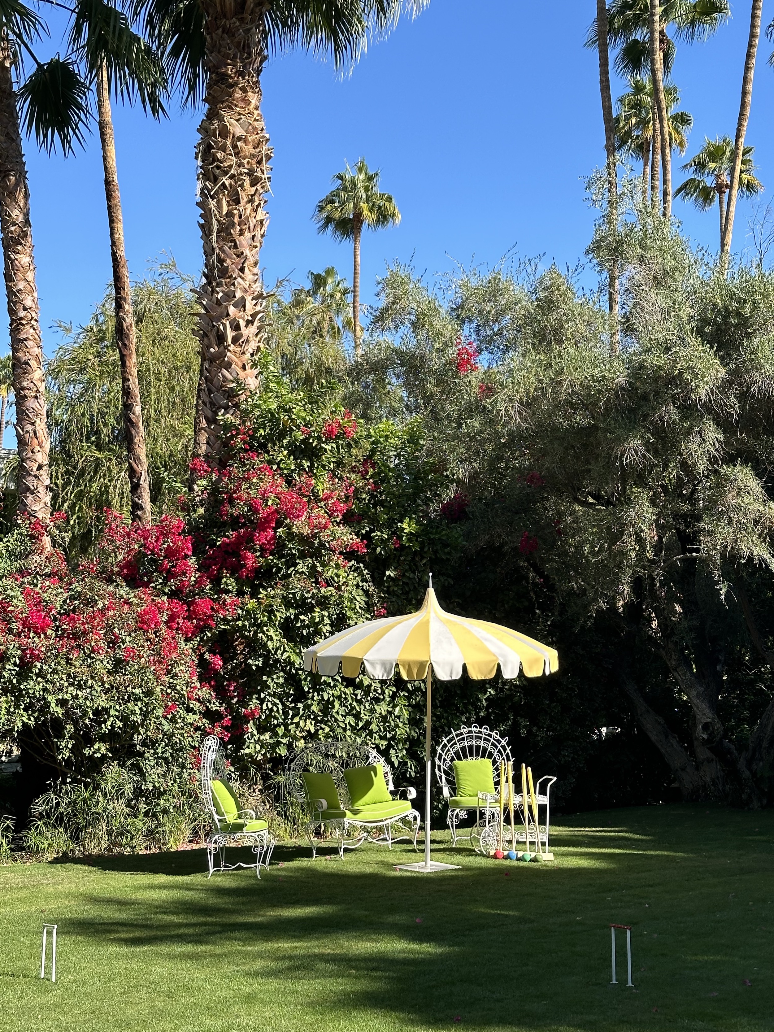 A yellow and white striped umbrella and green chairs on the croquet lawn at Parker Palm Springs