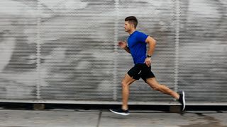 A man in a blue shirt is running past some some store shutters