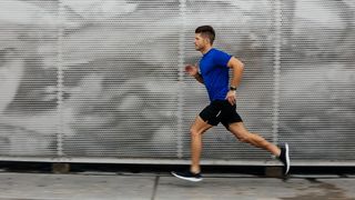 A man in a blue shirt is running past some some store shutters that are sprayed with graffiti