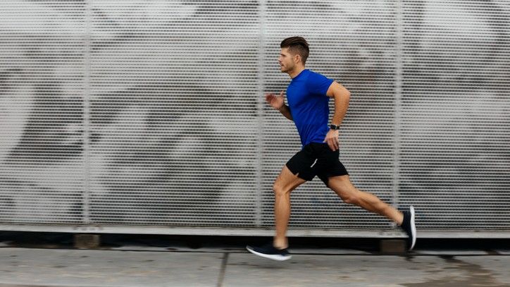 A man in a blue shirt is running past some some store shutters