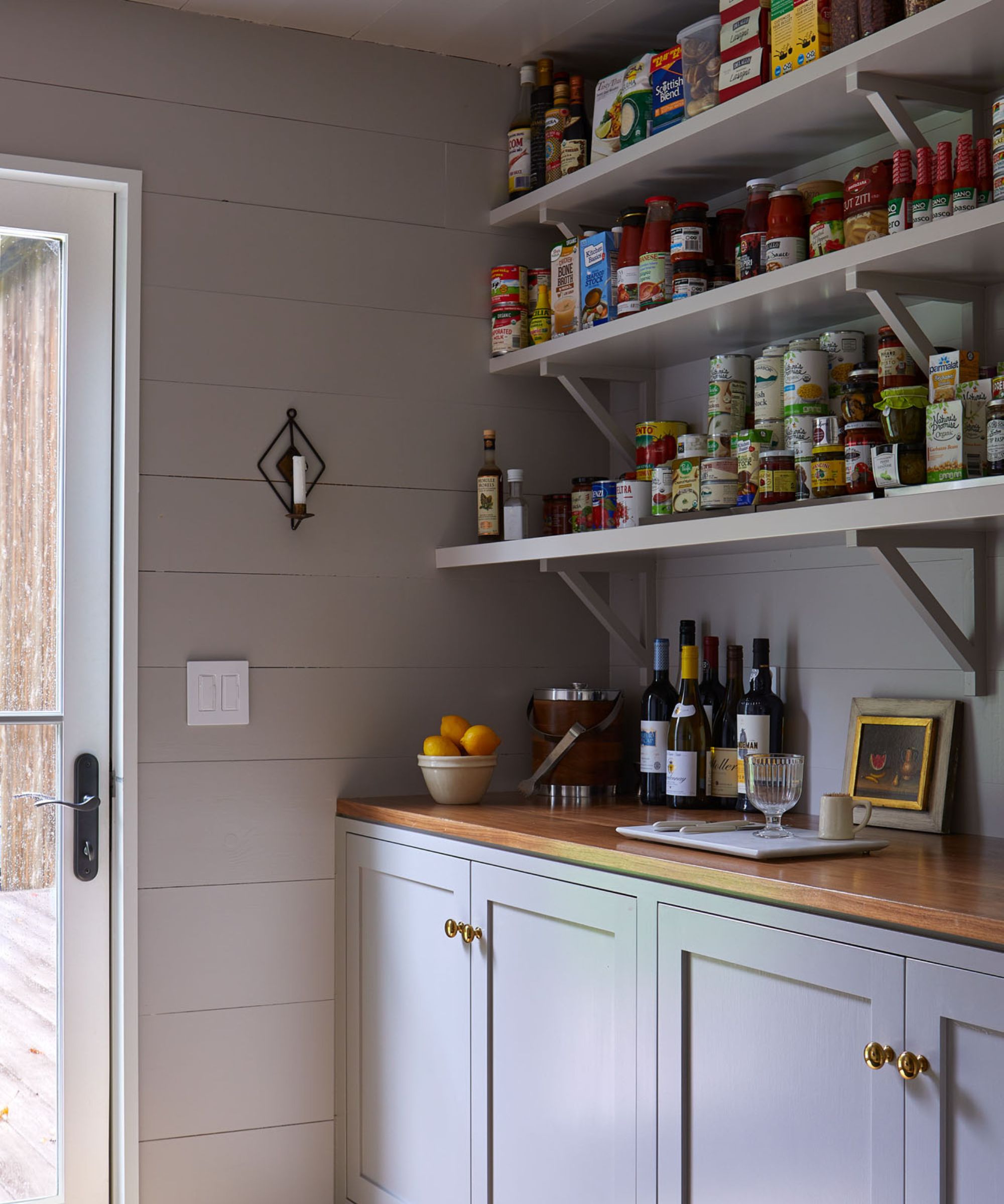 A country pantry with paneled walls, open shelving, wooden countertops, and Shaker cabinets