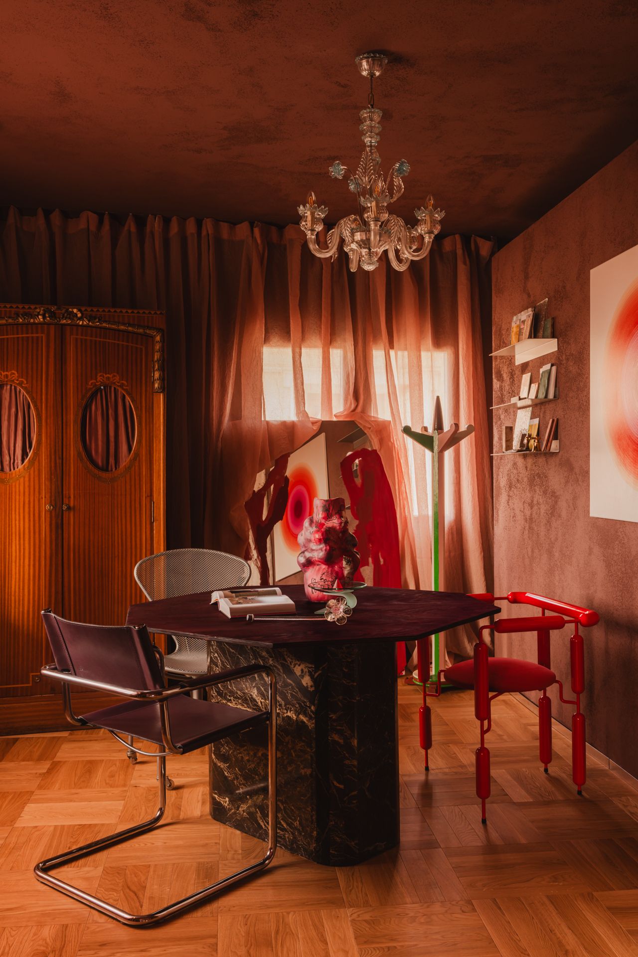 A geometric table is used as a desk in this work area, with three different chairs encircling the surface beneath a glass chandelier.