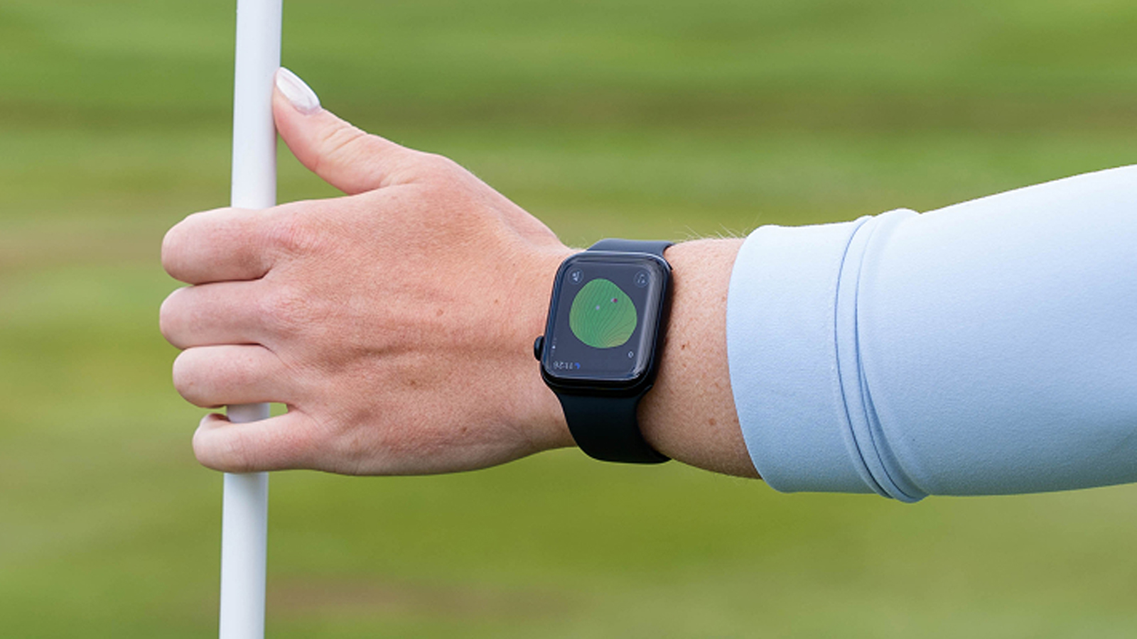 A golfer puts a flag in the hole while wearing an Apple Watch