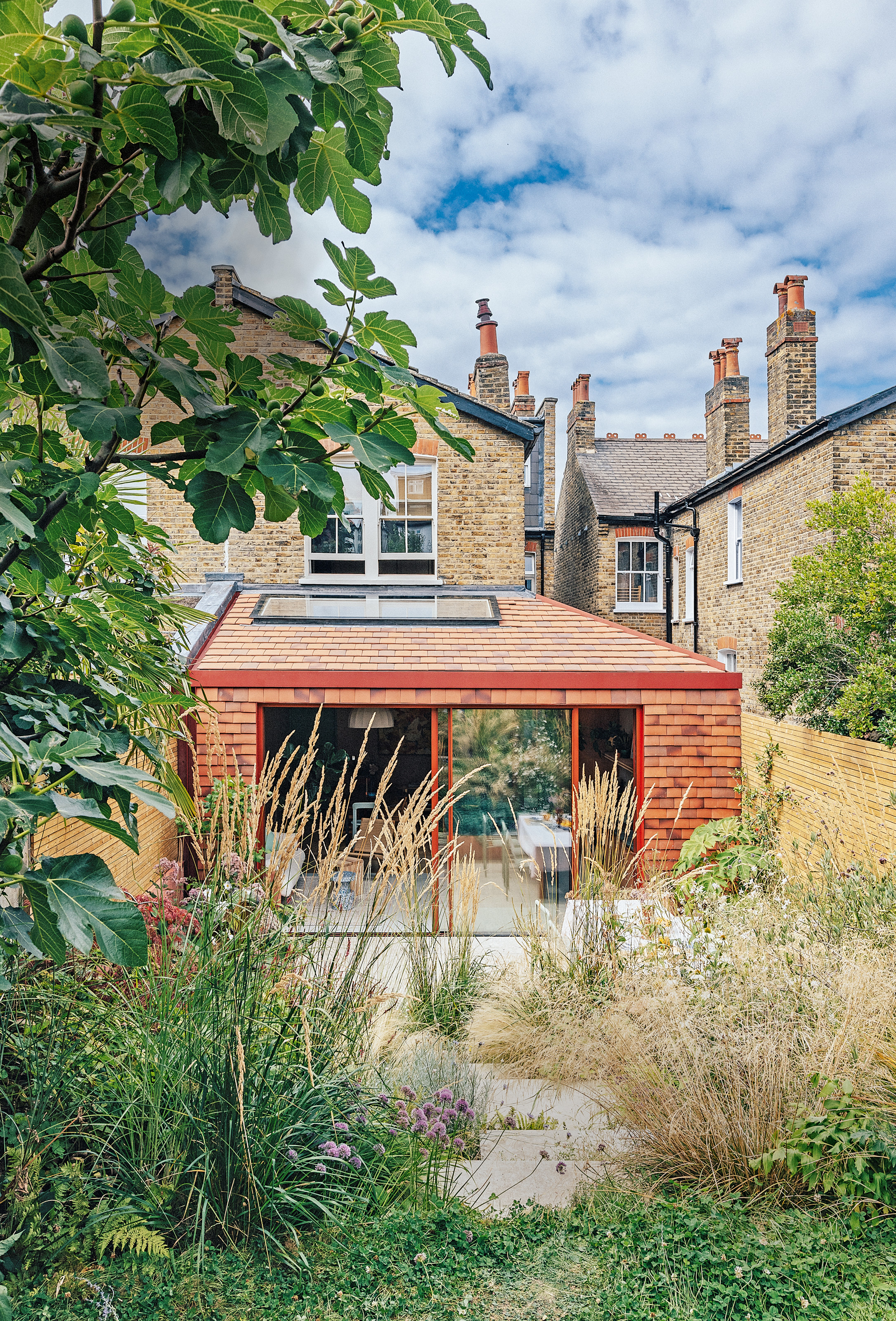Extension to house with red slate tiles, red-framed sliding doors and contemporary planted garden with grey stone steps