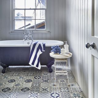 coastal bathroom with grey tongue & groove walls, blue bath, vintage metal side table, patterned blue and white floor tiles