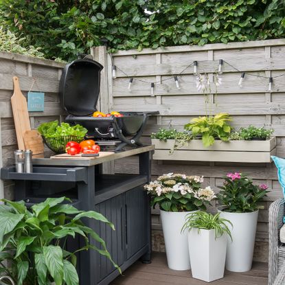 Corner of garden with tabletop BBQ, festoon lighting and potted plants