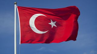 The flag of Türkiye flying against a blue sky