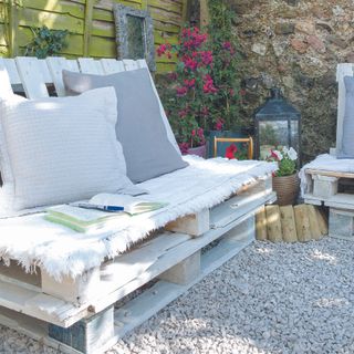 White pallet in a garden being used as a chair with pillows.