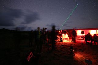 a dark sky full of stars and a green laser pointer stretching out into the sky.