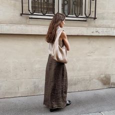 A woman wears a gray tank, brown skirt, and suede shoulder bag.