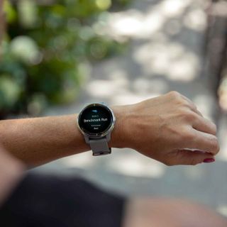 A man's arm is shown as he wears a smartwatch outdoors against a blurred background.