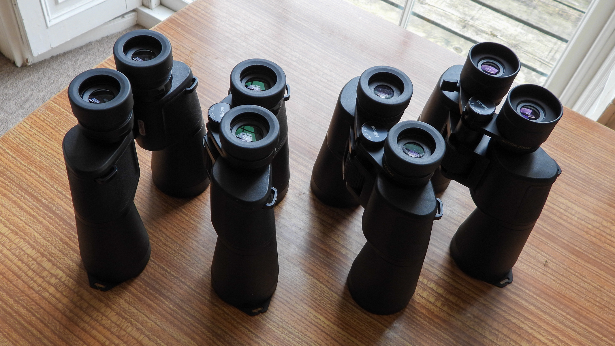 From left to right: the Nikon Action 7x50, Nikon Action 10x50, Nikon Action 16x50 and Nikon Action Zoom 10-22x50 binoculars lined up on a wooden table.