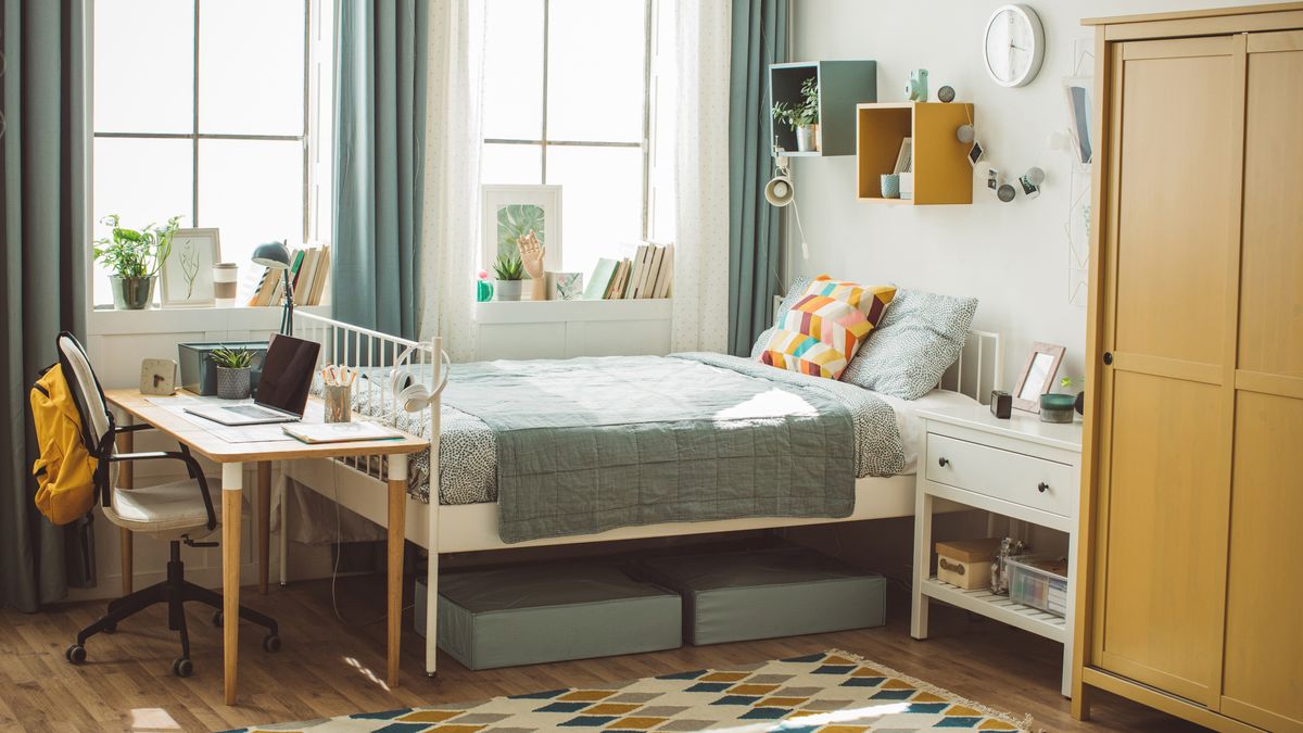 Image shows a brightly colored dorm room with a clean and comfy mattress placed on a white bedframe and dressed with brightly coloured cushions and a grey throw 