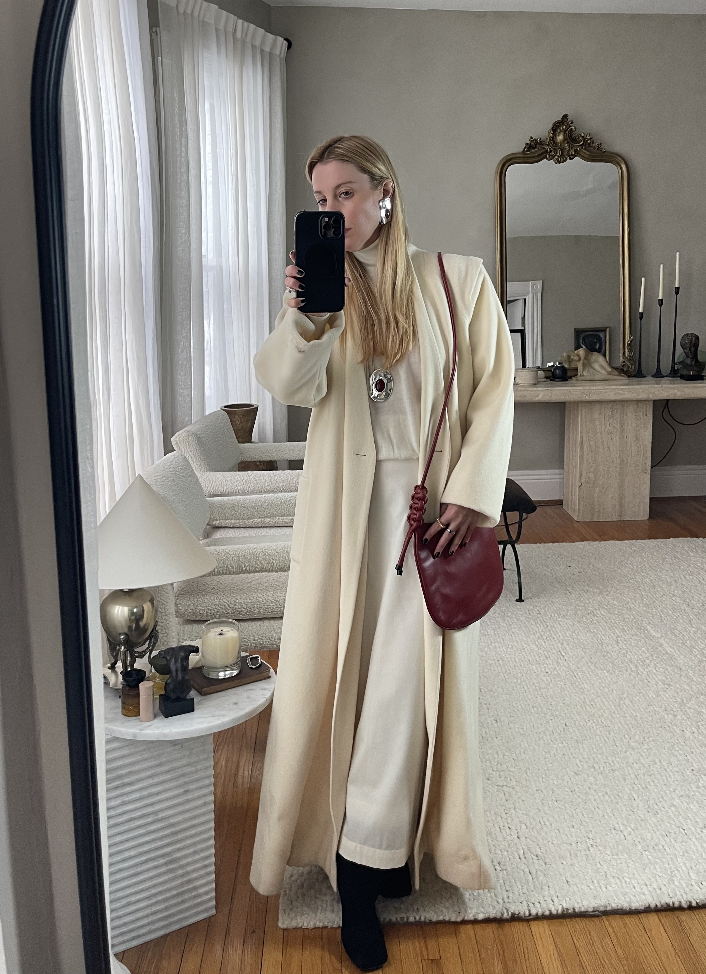 Kerry Pieri in a white set, white coat, black boots, and red crossbody bag